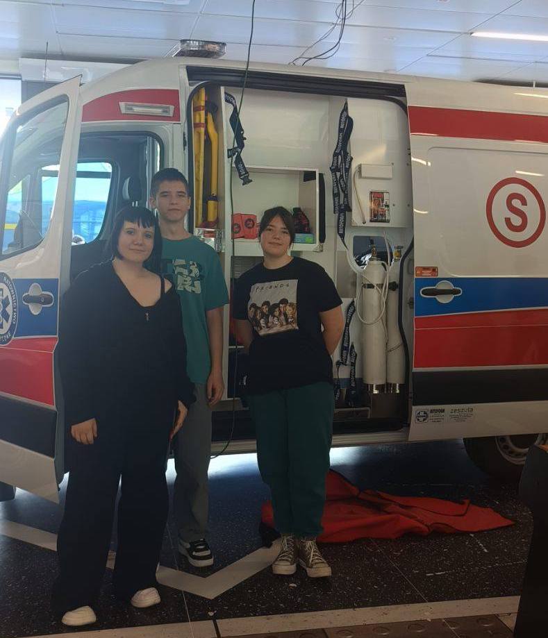 Na zdjęciu członkowie zespołu ratownictwa medycznego na tle karetki pogotowia ratunkowego.